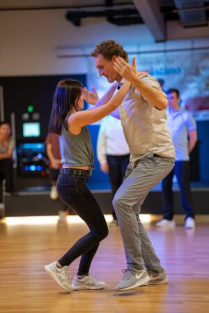 Mann und Frau tanzen Salsa in Ulm. Sie stehen sich gegenüber und konzentrieren sich auf den Tanz. Im Hintergrund verfolgen andere den Tanzkurs in der Tanzschule Ritmo Latino®.