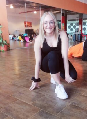Blonde Frau sitzt auf dem Boden und trägt Reggaeton-Tanzkleidung