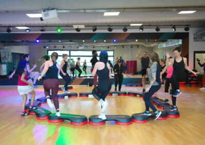Eine Gruppe von Männern und Frauen in Sportkleidung kreist um eine Fitnessmatte in der Tanzschule Ritmo Latino in Ulm. Im Hintergrund reflektiert ein großer Spiegel sein Bild.