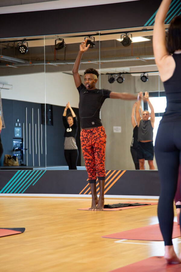 Eine Gruppe von Frauen und Männern trainiert Fitness in der Tanzschule Ritmo Latino in Ulm. In der Mitte streckt ein Mann seine Arme in Form eines „L“ aus. Im Hintergrund spiegelt ein Spiegel einige Teilnehmer wider.